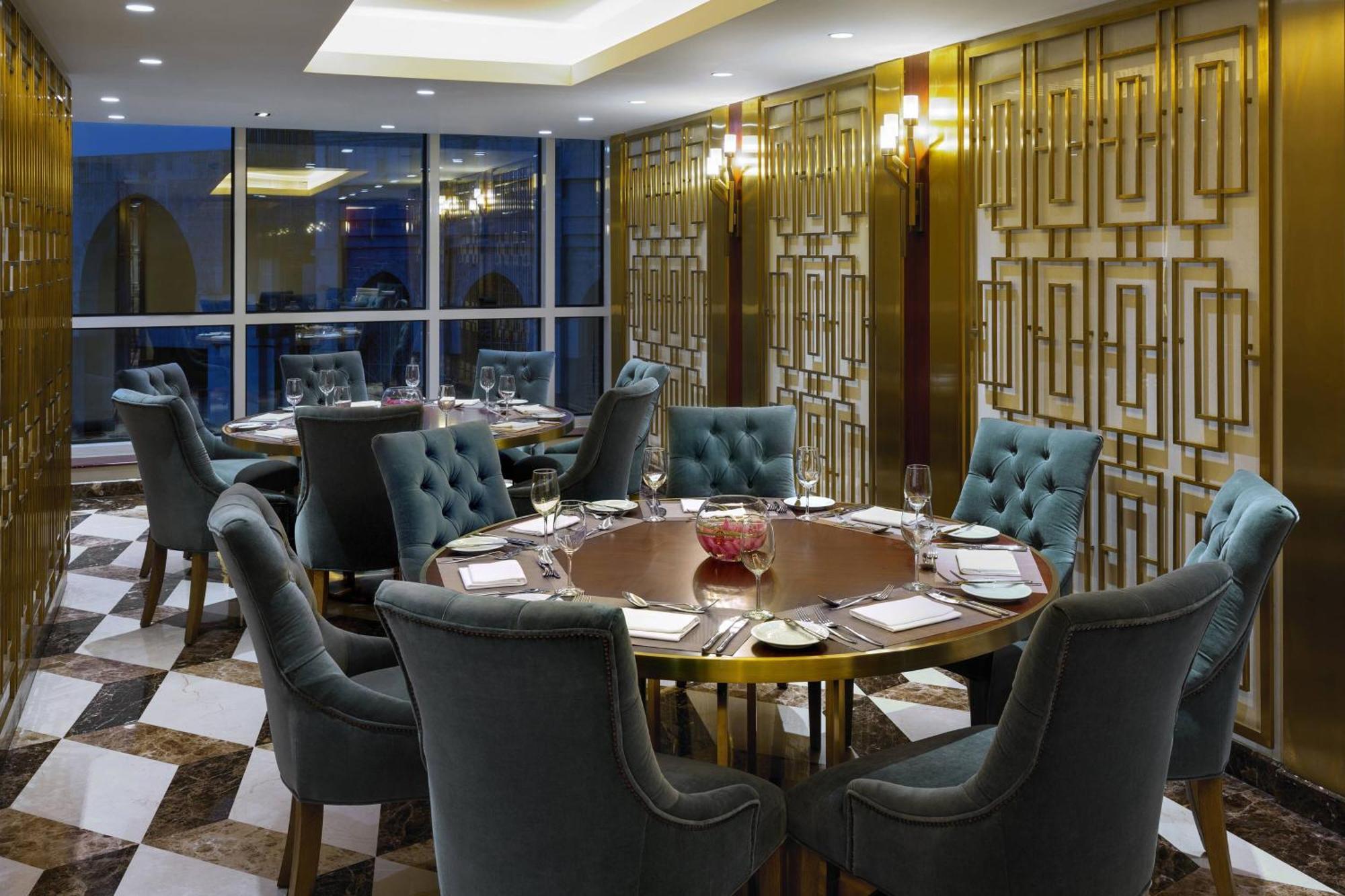 Sheraton Makkah Jabal Al Kaaba Hotel Мека Екстериор снимка The photo shows an elegant dining room with a sophisticated ambiance. It features a round wooden table at the center, surrounded by plush chairs upholstered in a soft, teal fabric. The room has a stylish décor, highlighted by a geometrically patterne