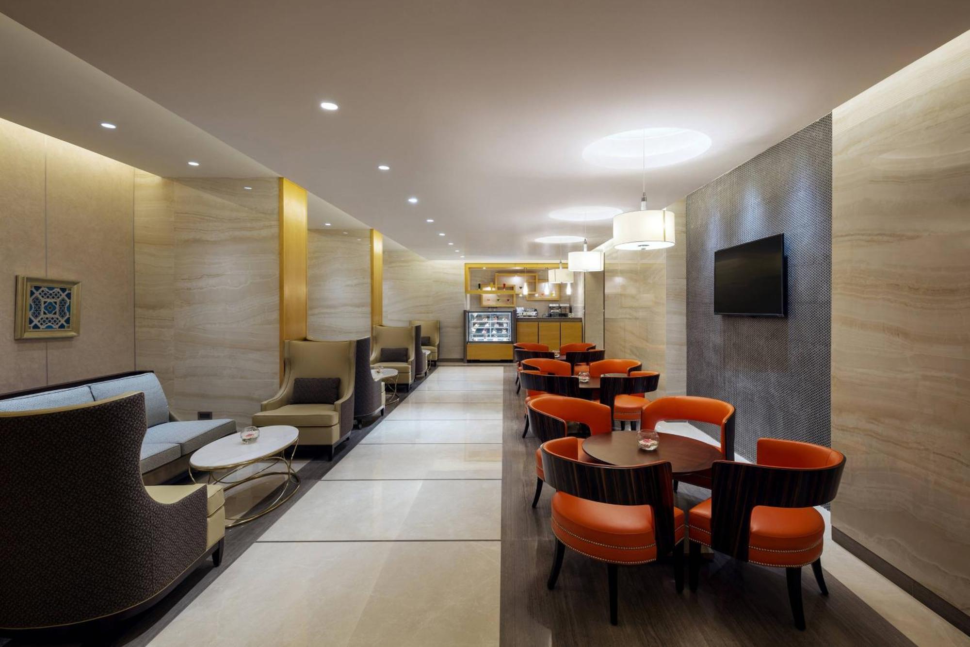 Sheraton Makkah Jabal Al Kaaba Hotel Мека Екстериор снимка The photo depicts a modern and elegant lounge or café area. The interior features soft, warm lighting and a combination of neutral and bold color schemes. On the left side, there are comfortable seating arrangements with light-colored sofas and chair